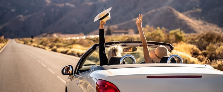 Zwei Frauen heben glücklich die Hände in einem Cabrio