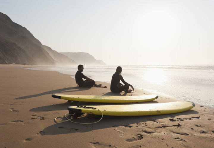 Paar sitzt am Strand neben ihren Surfboards